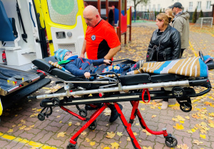 Dziecko transportowane do karetki przez pracownika karetki pogotowia.